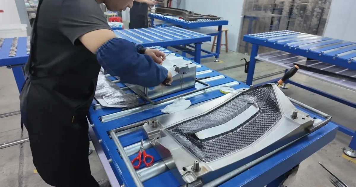 Technician hand-finishing a carbon fiber automotive part before quality inspection.